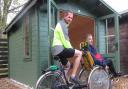 Volunteers with Bike Active Karl Rolfe (pedalling) and Steve Dosher, outside the new log cabin at Alton Water
