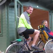 Volunteers with Bike Active Karl Rolfe (pedalling) and Steve Dosher, outside the new log cabin at Alton Water