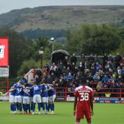 Town players in a pre-match huddle against the backdrop of the hills around Accrington.